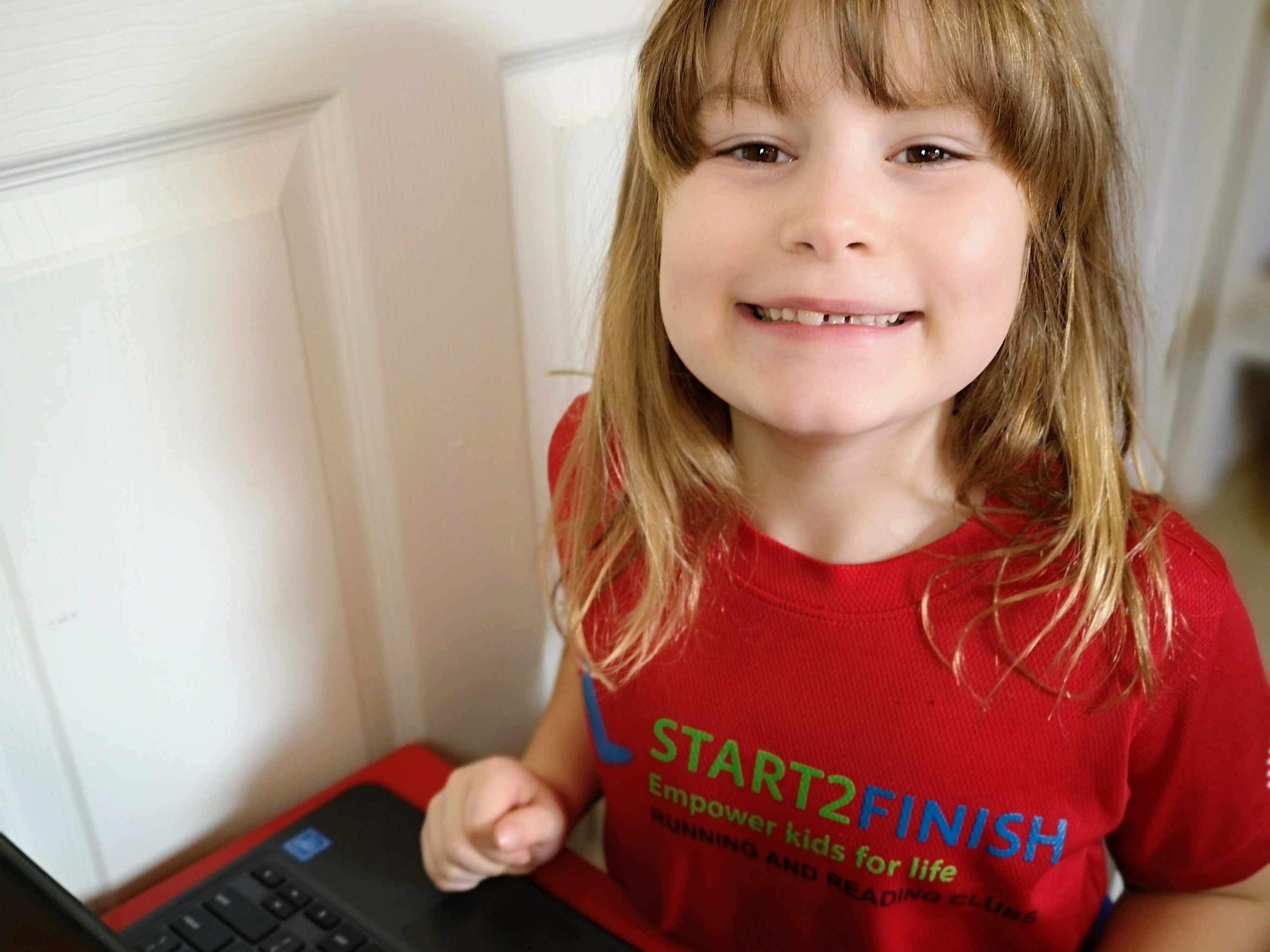 Child smiling at the camera while using a laptop
