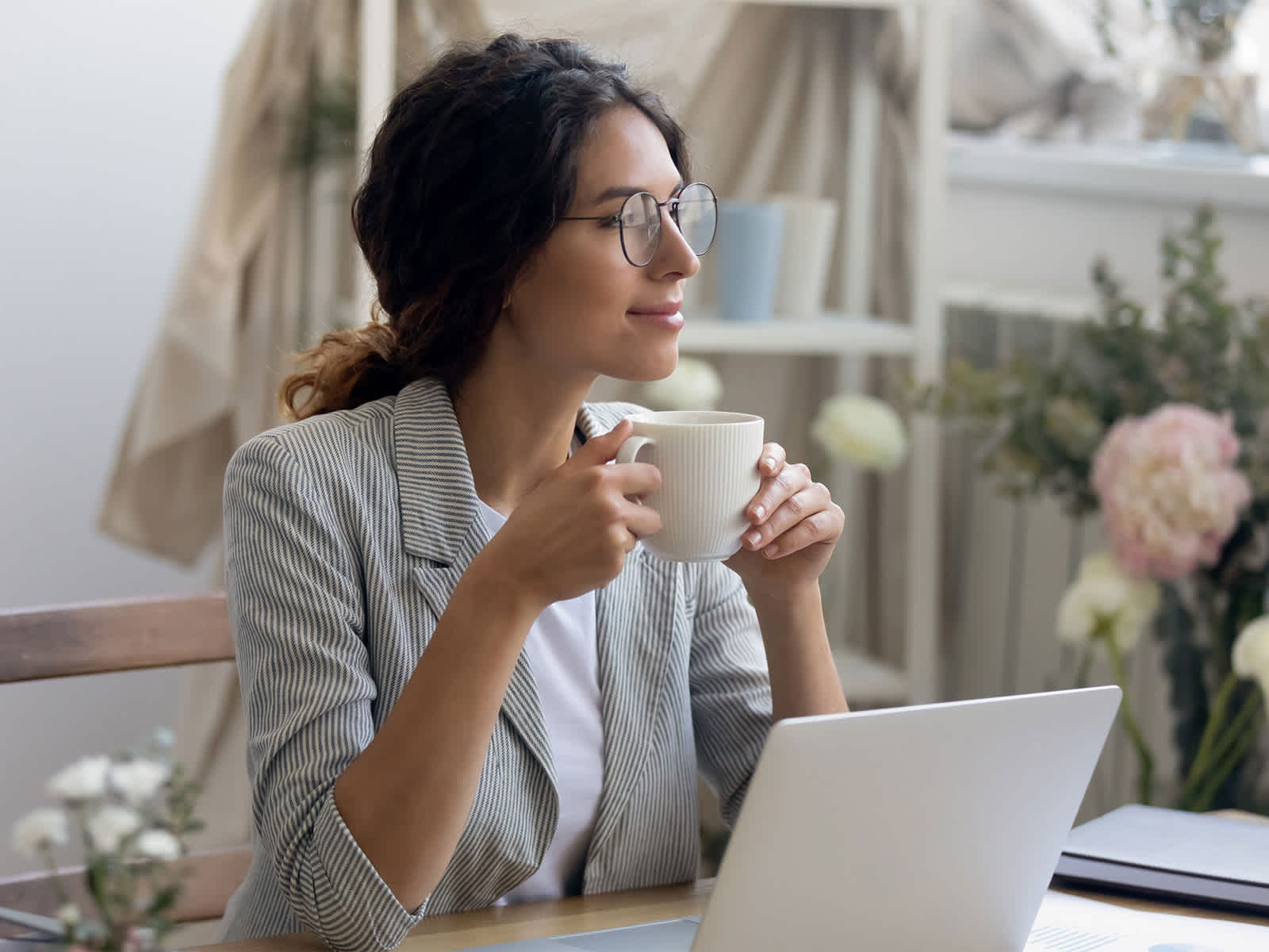 Une jeune femme d'affaires souriante en lunettes boit un café le matin dans son bureau à la maison.