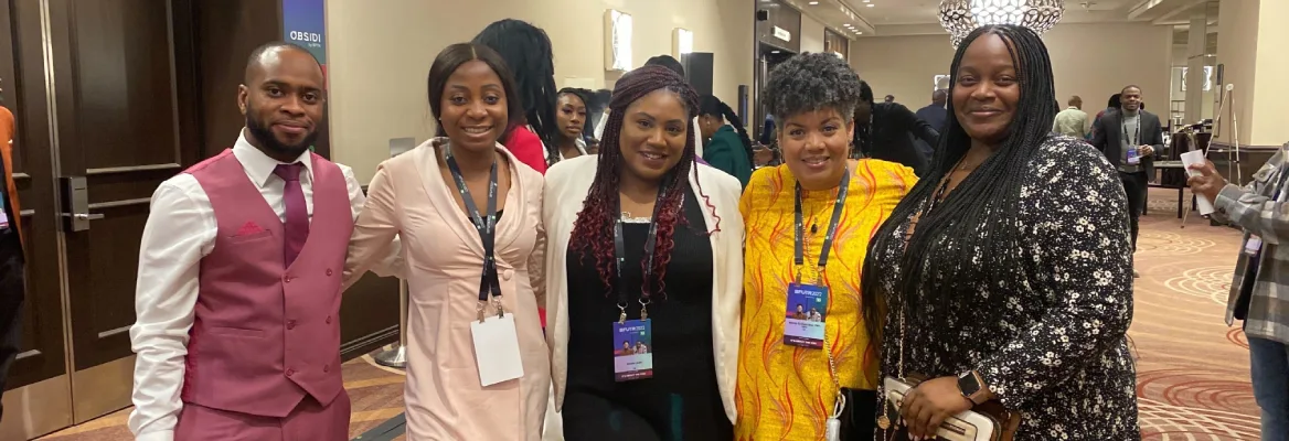 5 Black team members stand together at a conference, some wearing conference lanyards