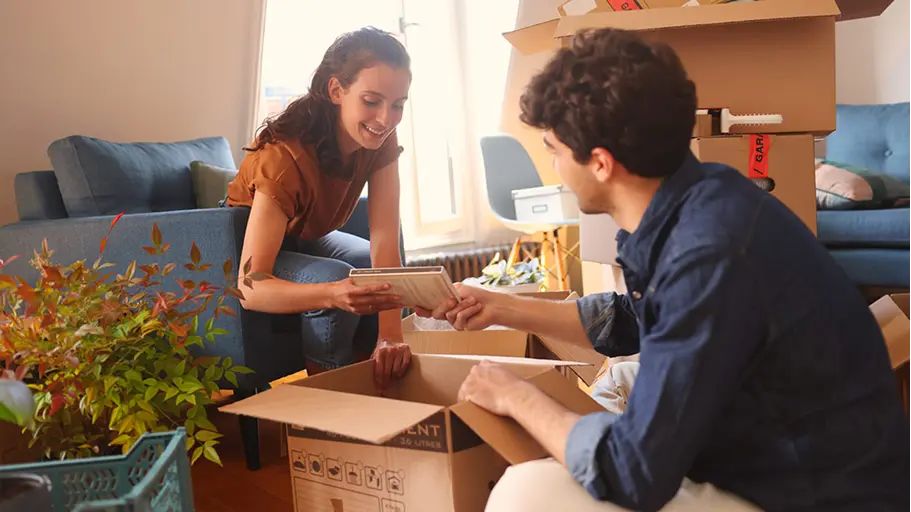Two people unpacking boxes in a living room, showing the potential of dust mite allergy indoors.