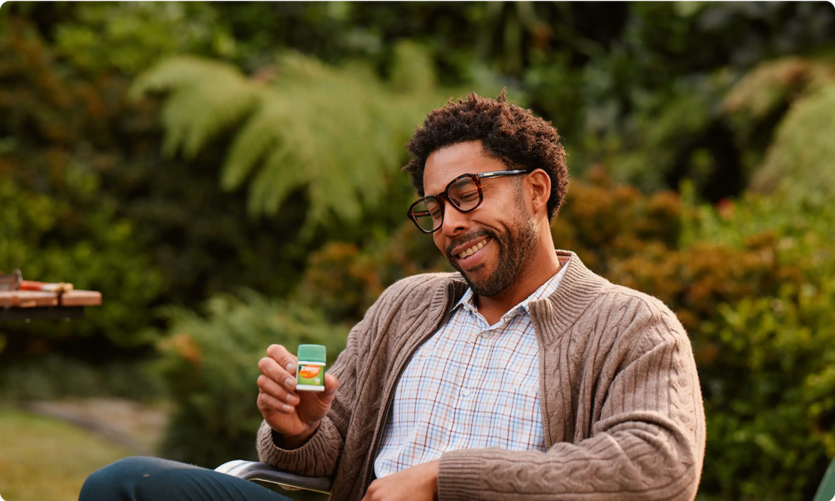A person sitting in a chair outside holding ZYRTEC® Allergy Relief Medicine Tablets