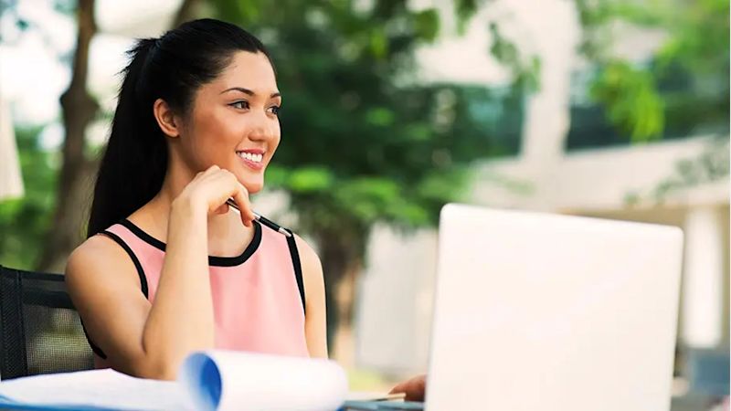 A woman sitting outside working on a laptop, representing the lifestyle of living with allergies.