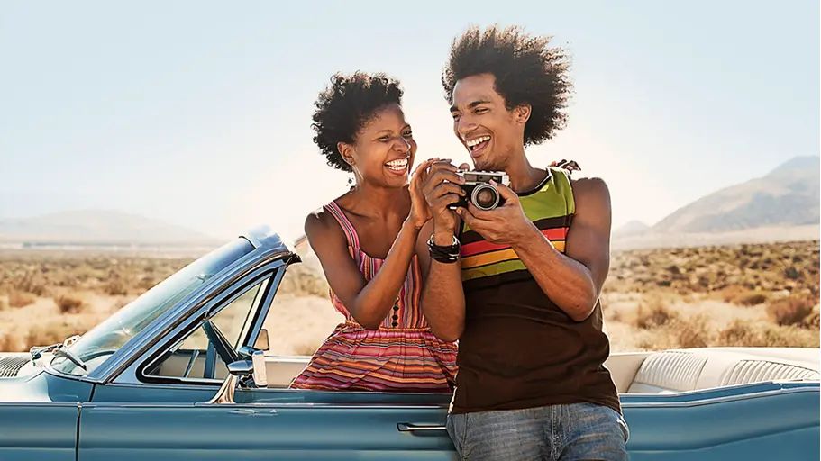 Two people outside in a covertible holding a camera