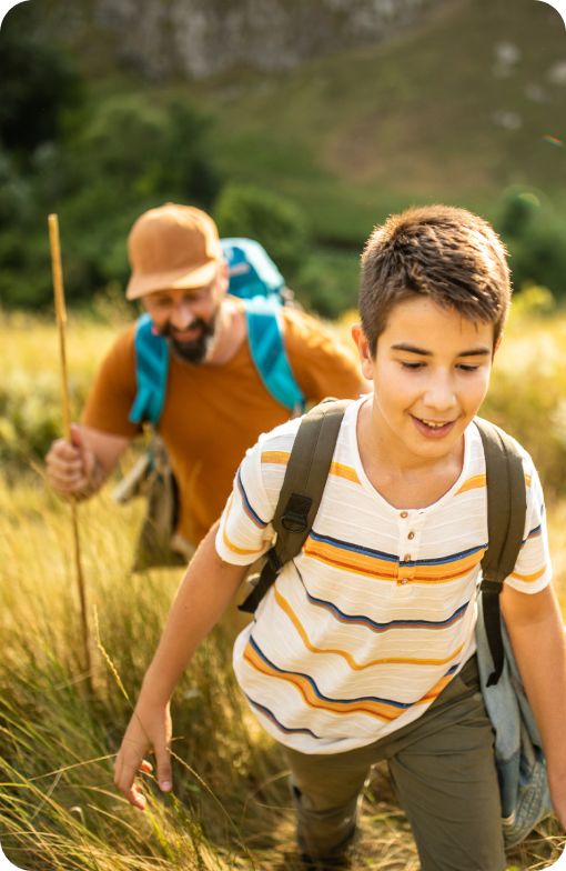 A man and a boy hiking outdoors, both carrying backpacks, suggesting preparedness and adventure.