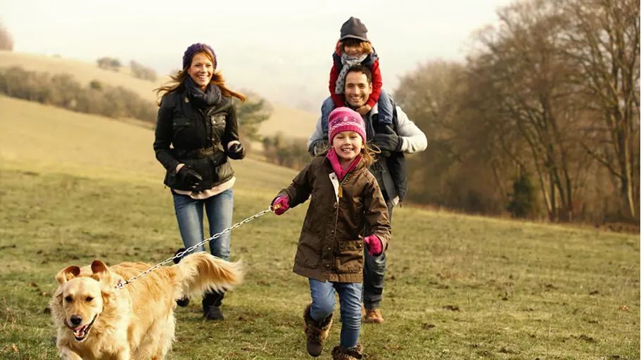 A family bundled up outside with their dog in a field during the winter