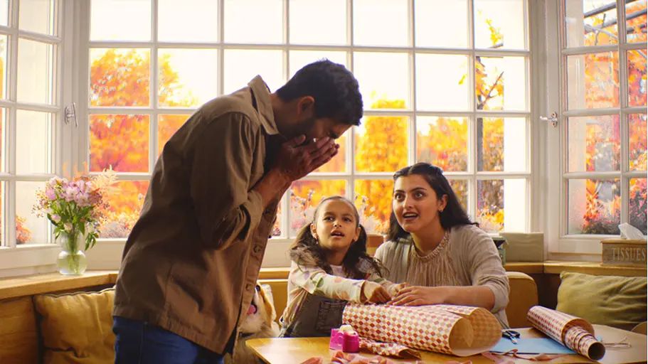 A person sneezing with their family wrapping gifts in the background
