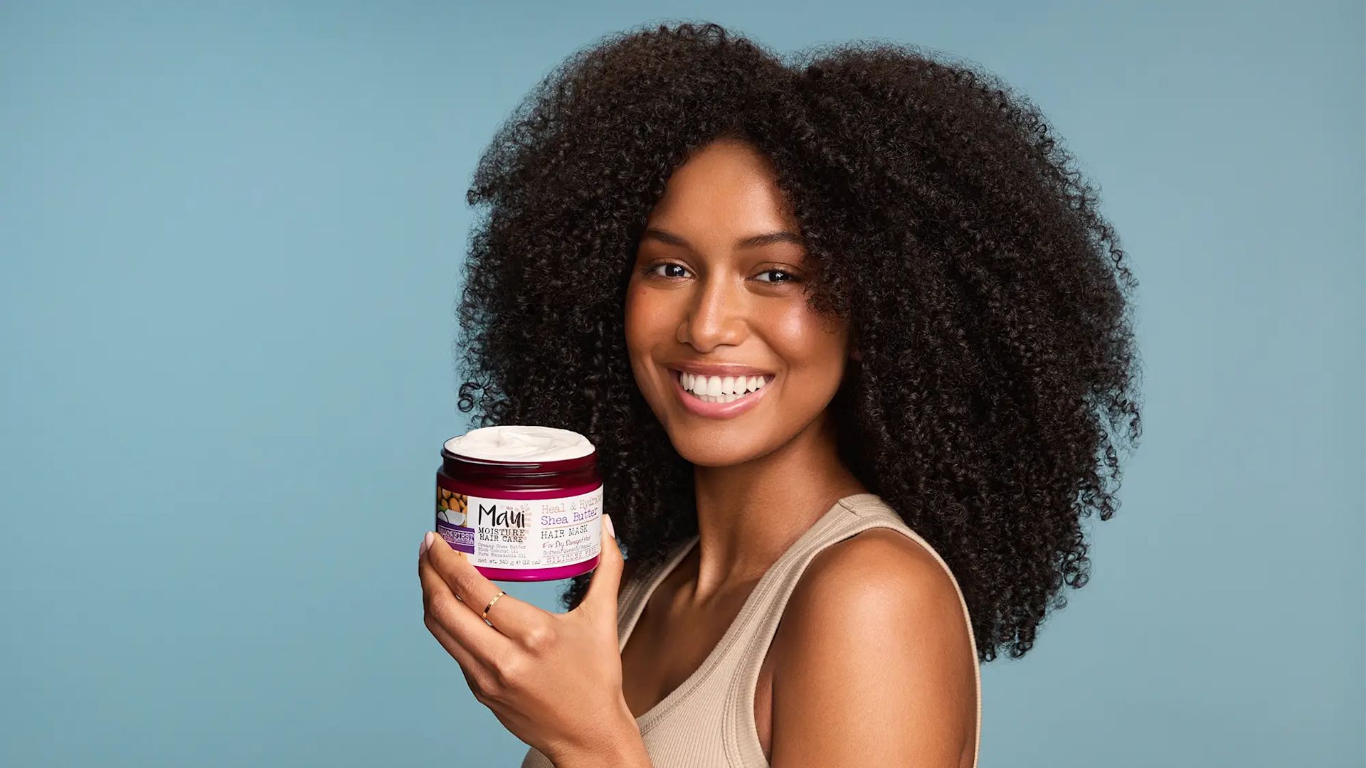 Woman with healthy curls holding Maui Moisture Shea Butter Hair Mask