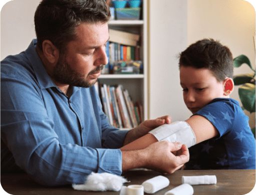Man placing a bandage over a small boy’s wounded elbow.
