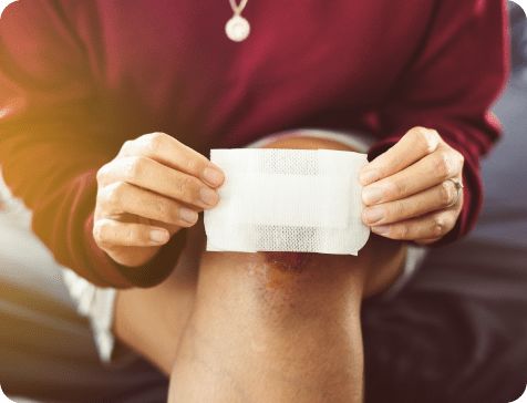 Person placing an adhesive bandage on a large cut on their knee.