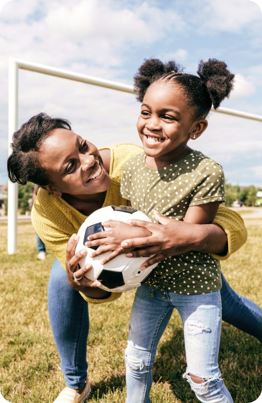 Mother playing outside with a soccer ball with her daughter.