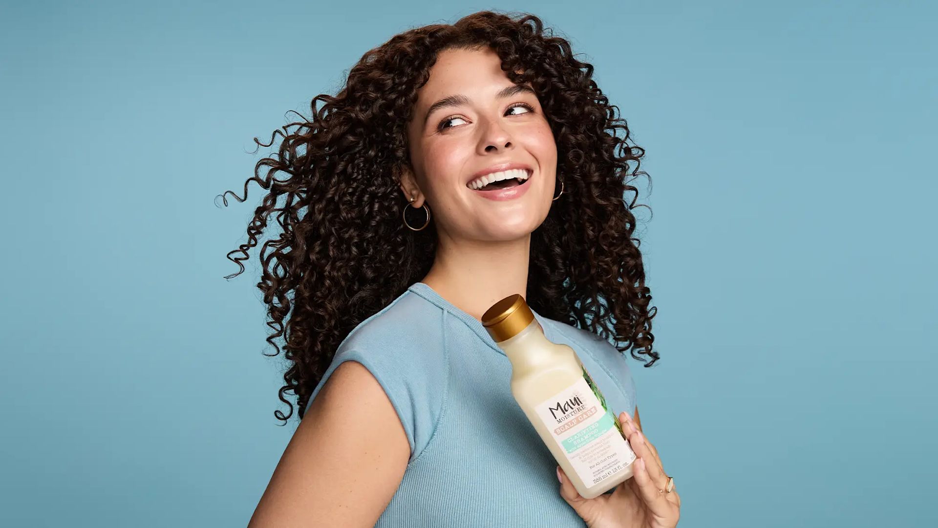 Smiling Woman with healthy curls holding Maui Moisture Scalp Care Clarifying Shampoo