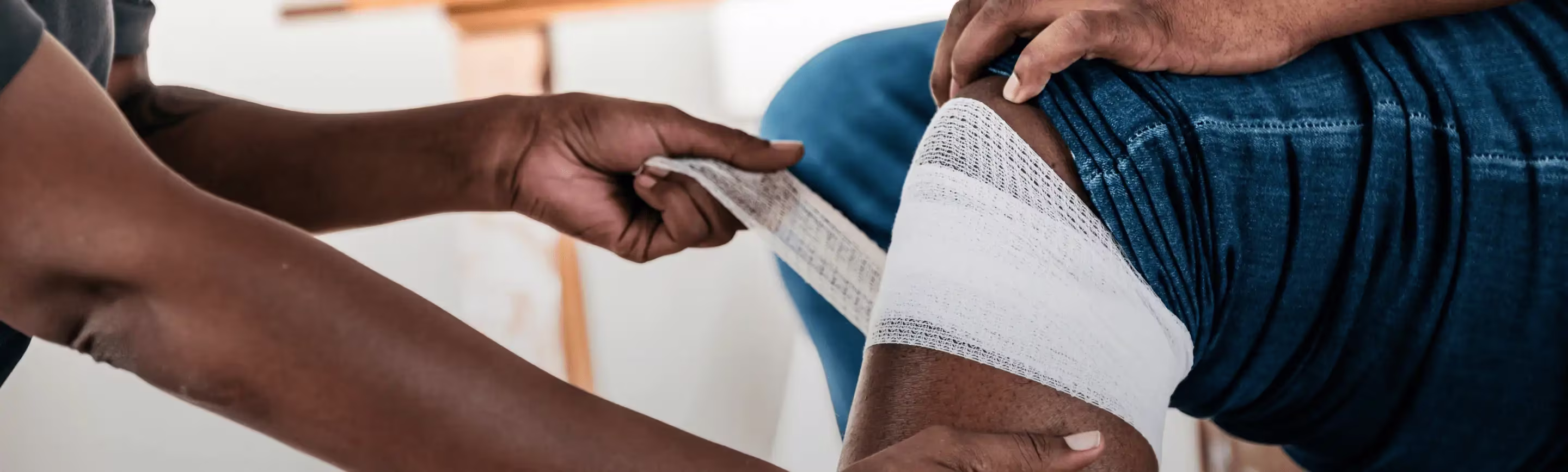 Person using BAND-AID® Brand Gauze to wrap a wound on a knee.