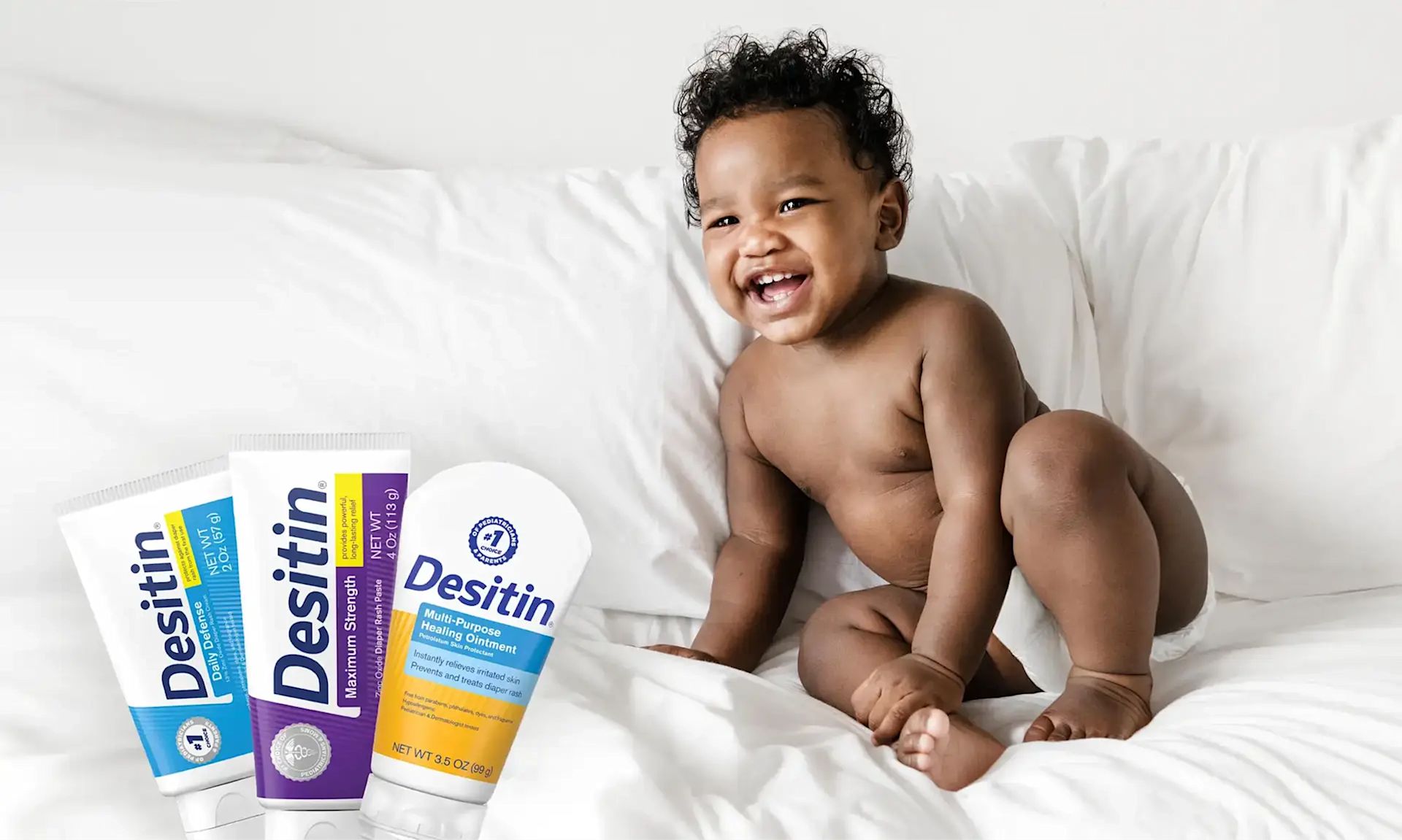 Desitin® Product Collection banner, a baby radiantly smiling when sitting on the comforter