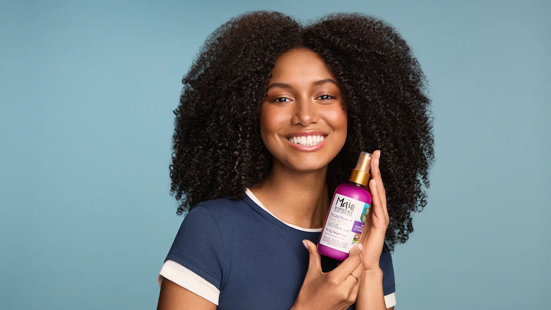 Woman with healthy curls holding Maui Moisture Shea Butter Leave In Mist