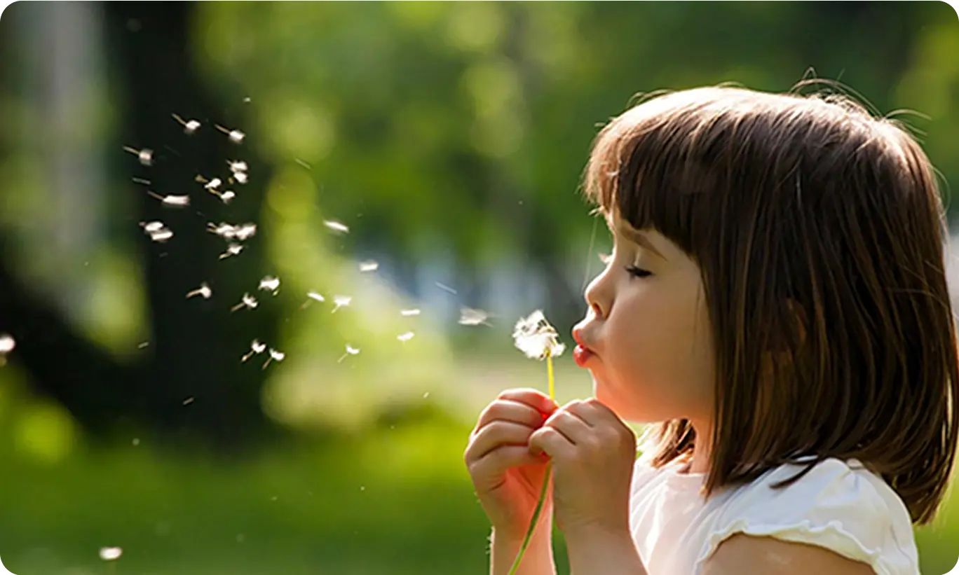 A child blowing on a dandelion, highlighting common triggers of kid's allergies during outdoor play.