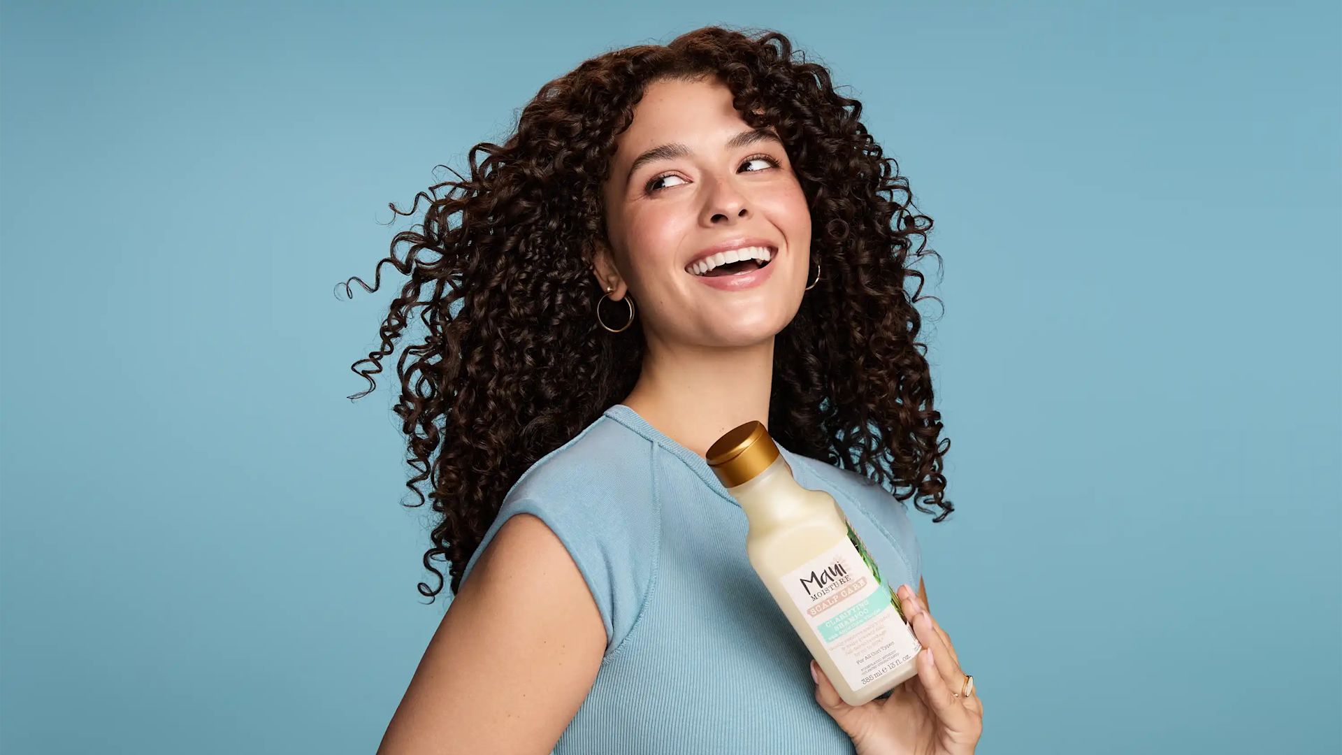 Smiling woman with curly hair holding Maui Moisture Scalp Care Clarifying Shampoo