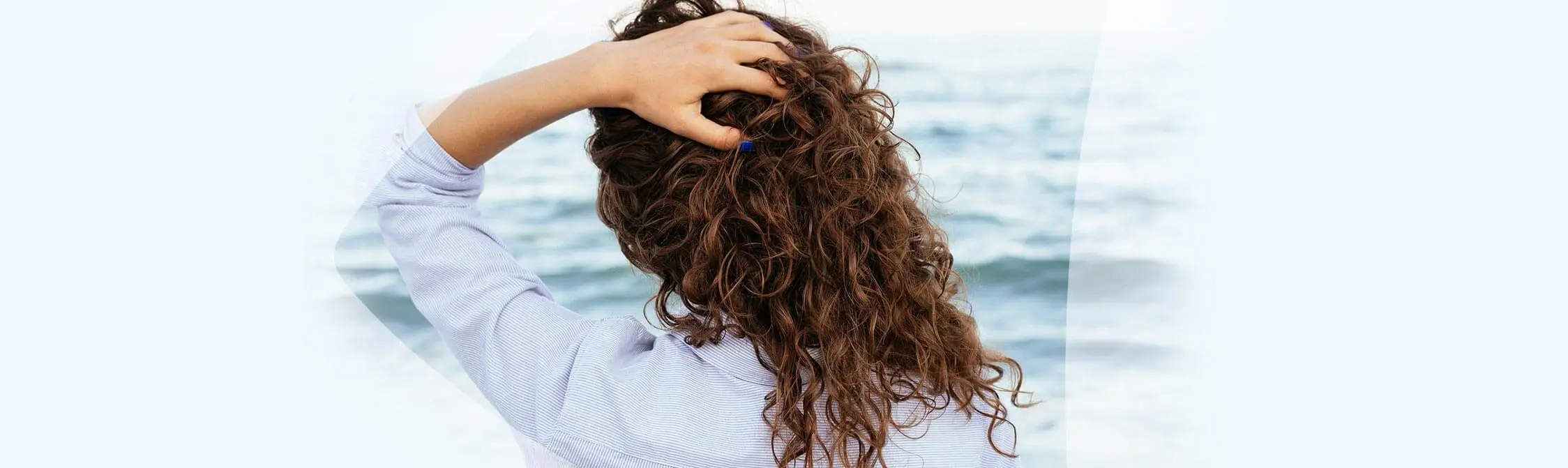 Vrouw met de handen in het haar kijkt over de zee uit