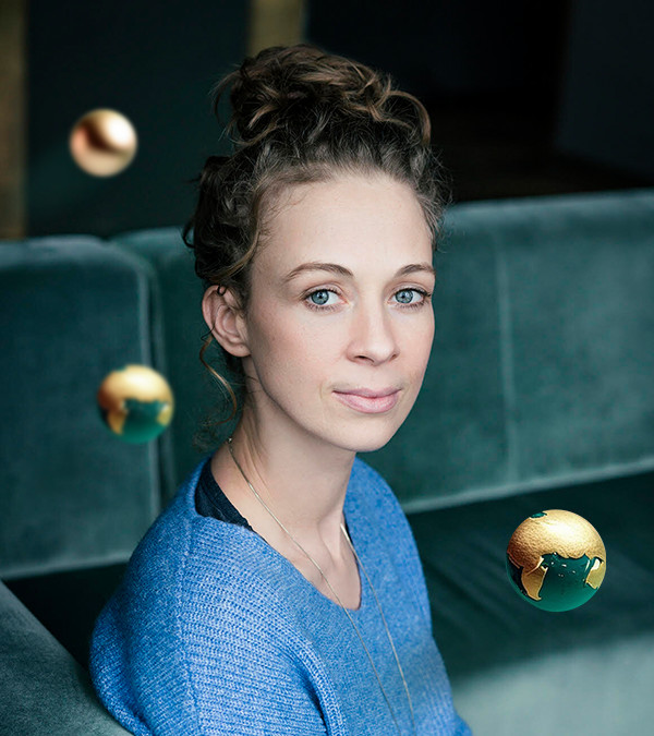 Helena Steinhaus schaut in die Kamera, umgeben von drei gold-grünen Weltkugeln