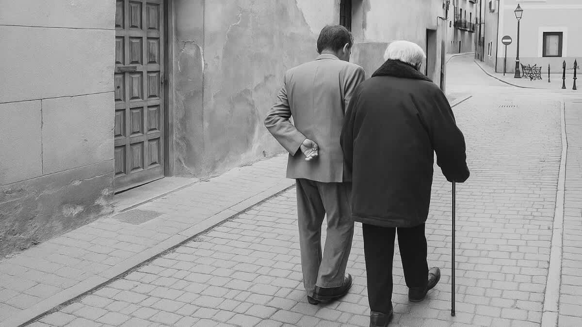 Schwarzweißfoto von zwei alten Menschen, die man von hinten beim Spazierengehen in einer Gasse sieht.