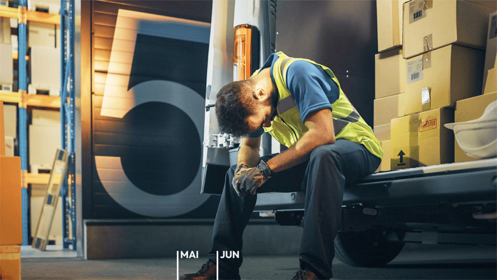 Paketfahrer sitzt erschöpft auf der Ladekante seines voll beladenen Vans