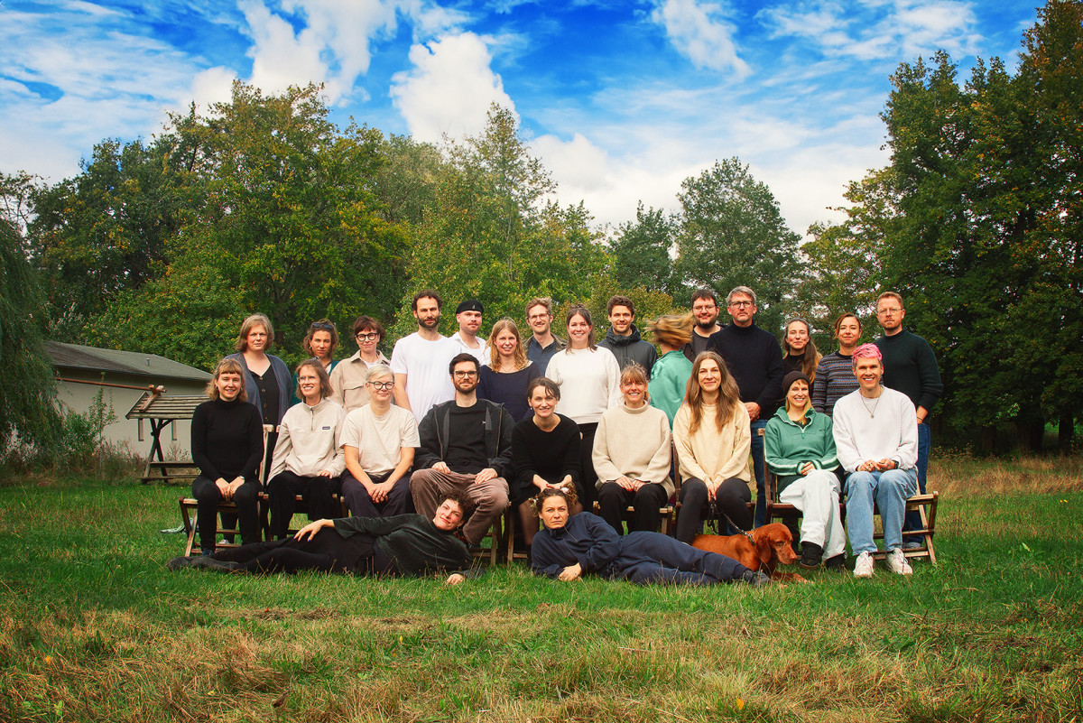 Die Teammitglieder des Vereins Mein Grundeinkommen e.V. posieren auf einer spätsommerlichen Wiese vor blauem Himmel für ein Gruppenbild.