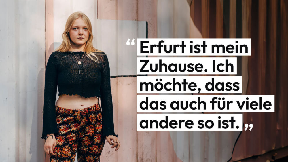 Ianthe steht vor einem mit Graffiti besprühten Container. Sie sagt: 