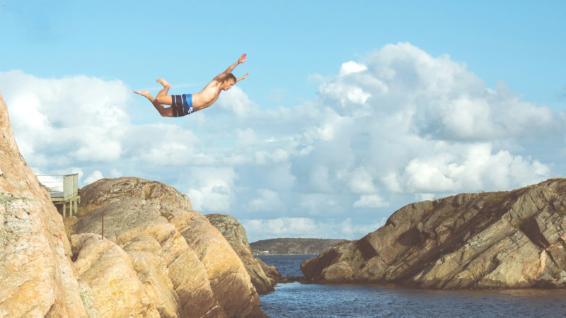 Eine Person springt von einer Klippe ins Meer.