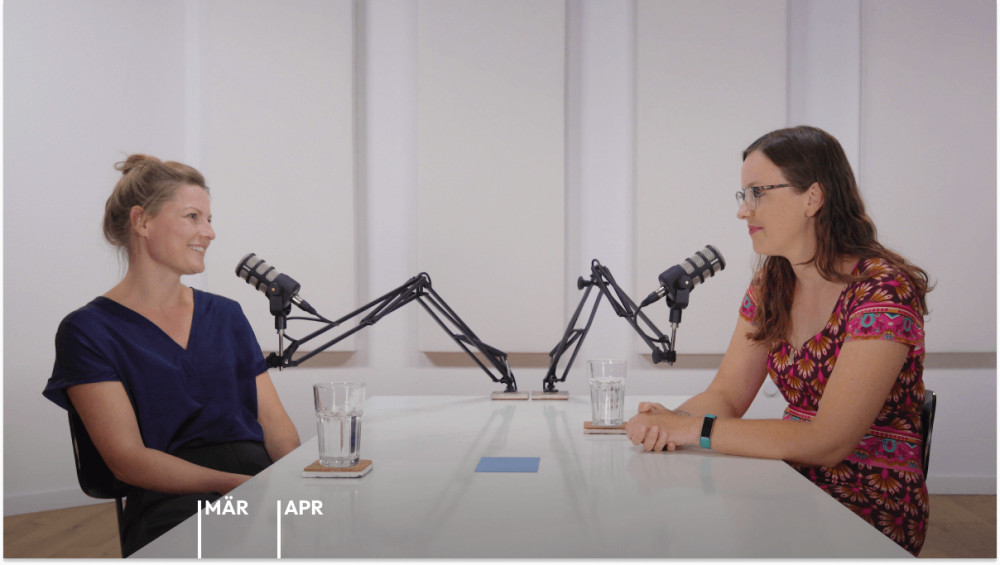 Prof. Dr. Susann Fiedler und Helene Bockhorst sitzen sich lächelnd an einem Tisch mit Mikrofonen gegenüber