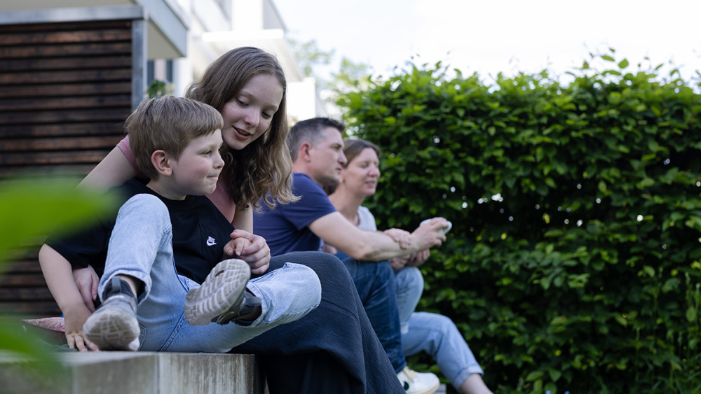 Eine vier-köpfige Familie sitzt auf der Kante ihrer Terrasse. 