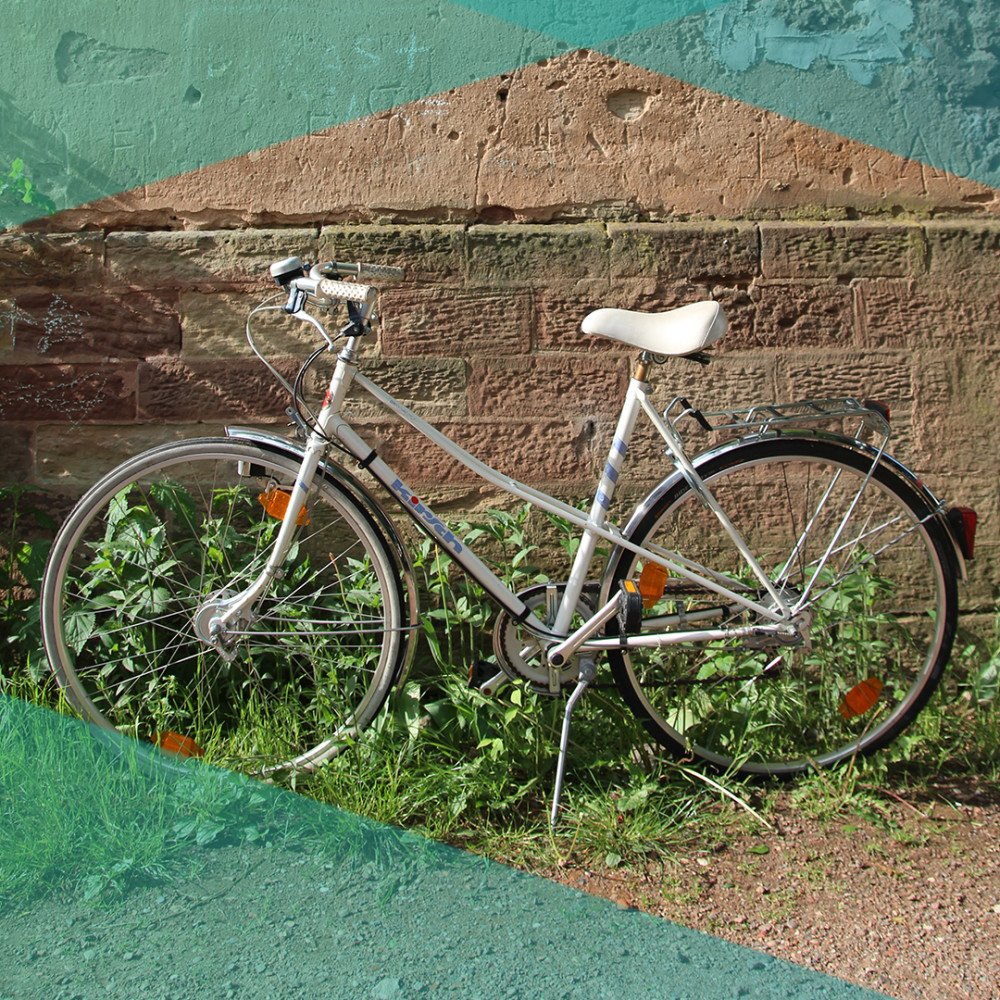 Ein weißes Damenrad steht vor einer sonnenbeschienenen Backsteinwand. 