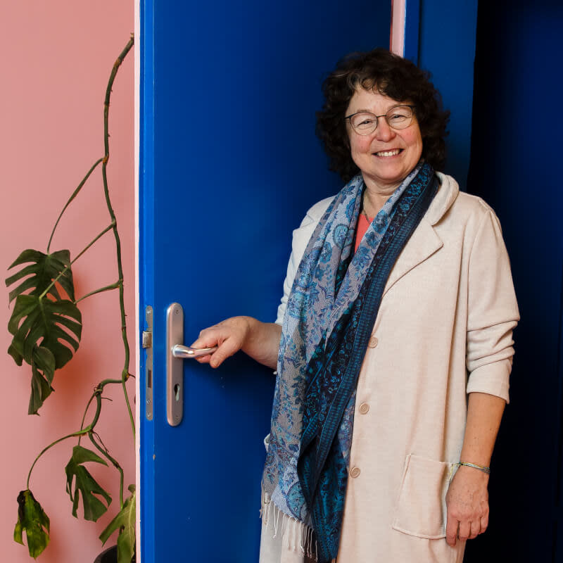 Luzia öffnet eine blaue Tür und guckt dabei freundlich in die Kamera. 