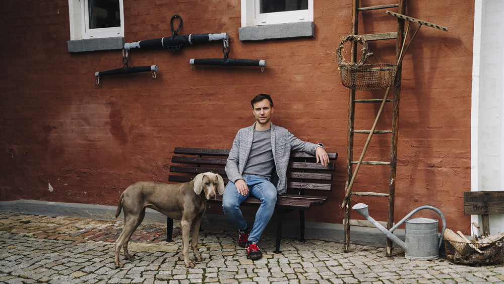 Der Protagonist Maik sitzt auf einer Bank vor einer Häuserwand. Neben ihm sein Hund. 