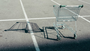 Ein leerer Einkaufswagen steht auf einem leeren Parkplatz und wirft einen Schatten auf den Asphalt.