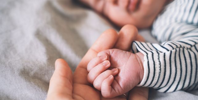 Die Hand eines Erwachsenen hält eine kleine Babyhand, während das Baby schläft.