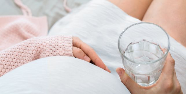 Schwangere Frau mit Wasserglas in der Hand.