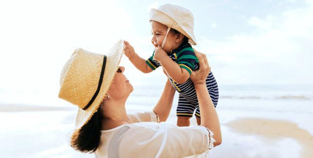 Mutter mit Baby mit Sonnenhut am Strand.