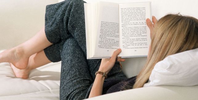 jeune femme allongée sur le canapé en train de lire un livre