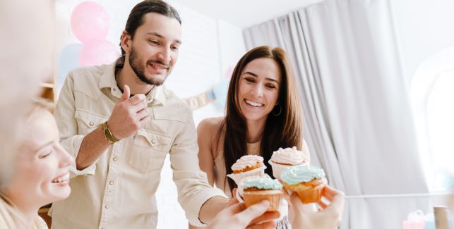 Paar mit Freunden feiert eine Gender Reveal Party mit Cupcakes.