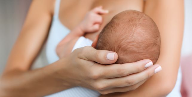 Frau hält Neugeborenes zum Stillen an ihrer Brust.
