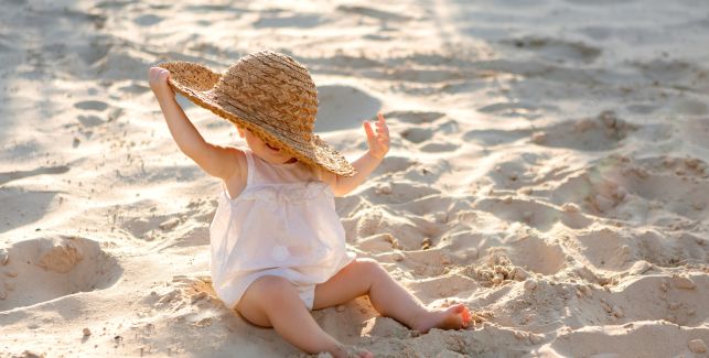 Baby im Kleid am Strand mit Sonnenhut.