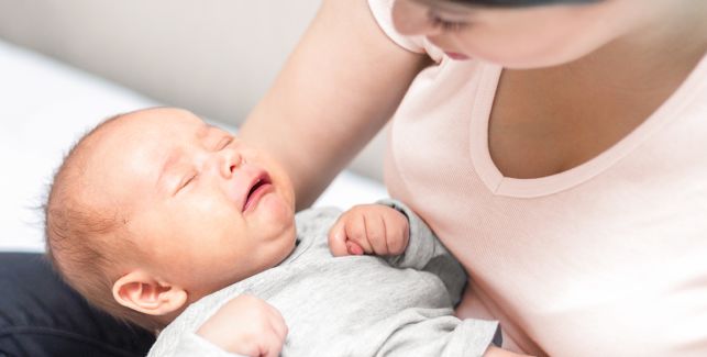 Eine Frau hält ein weinendes Baby mit schmerzverzehrtem Gesicht auf dem Arm.