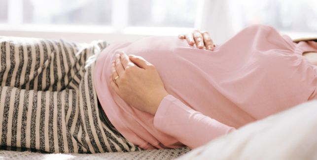 femme enceinte allongée dans son lit avec les mains sur son ventre