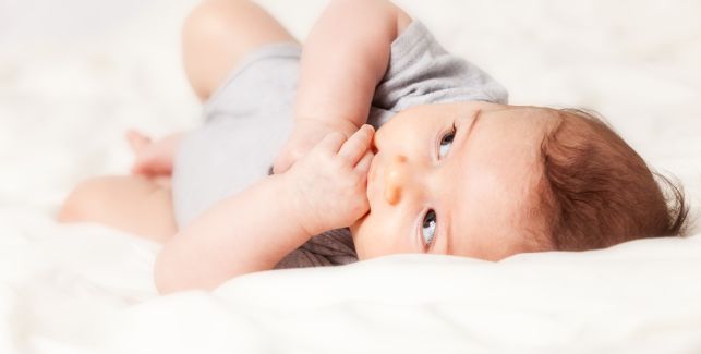 bébé allongé sur son lit avec les mains dans la bouche et les yeux ouverts