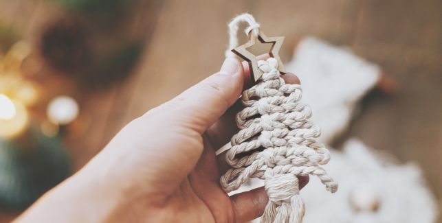 Frau hält einen aus Makramee geknüpften Baumschmuck in Form eines Weihnachtsbaums mit Stern.