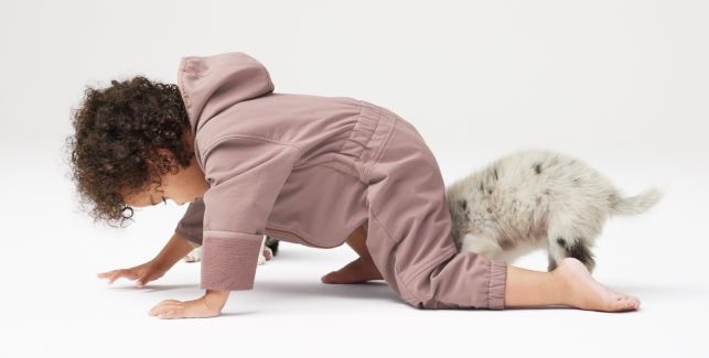 Kleinkind in gemütlicher Kinderkleidung krabbelt zusammen mit einem Haustier über den Boden.