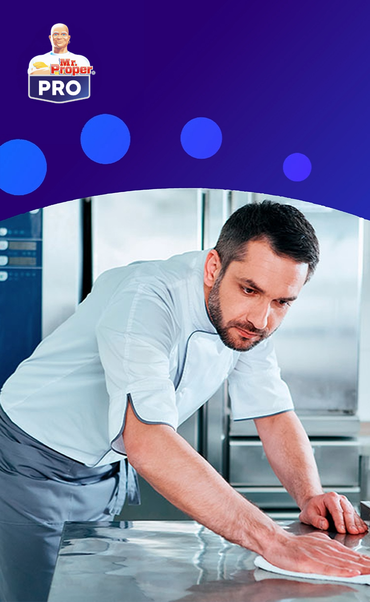 Een chef-kok maakt een roestvrijstalen werkblad schoon in een professionele keuken, met het Mr. Proper PRO-logo op een blauwe achtergrond.