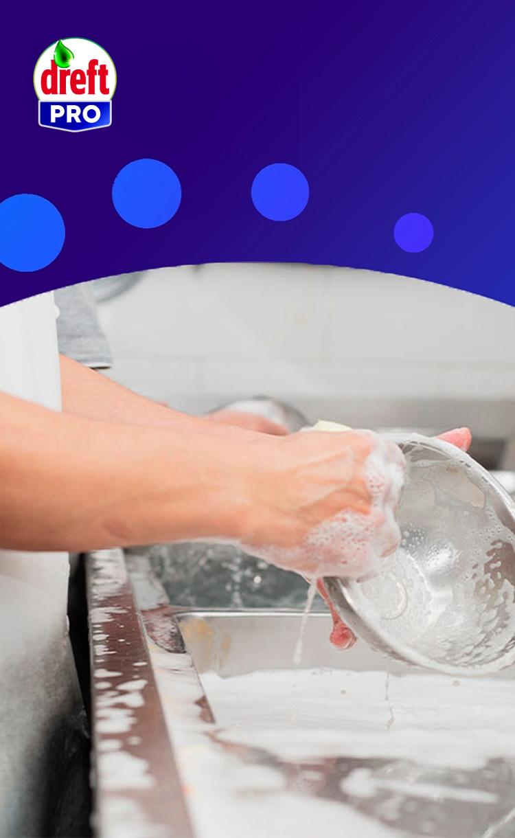 Gros plan sur des mains lavant un bol en métal plein de mousse dans un évier professionnel, avec le logo Dreft Pro à gauche.