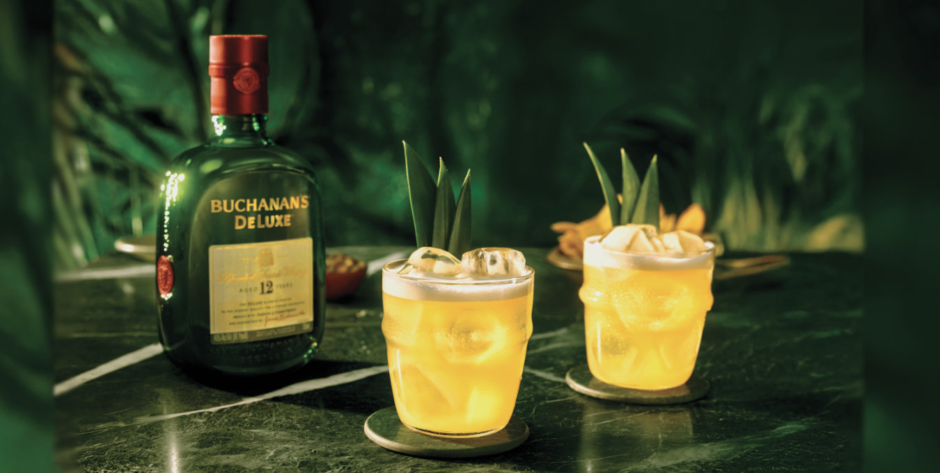 Two Buchanita cocktails on the rocks with pineapple garnish and a bottle of Buchanan's Deluxe Whiskey on a green marble counter