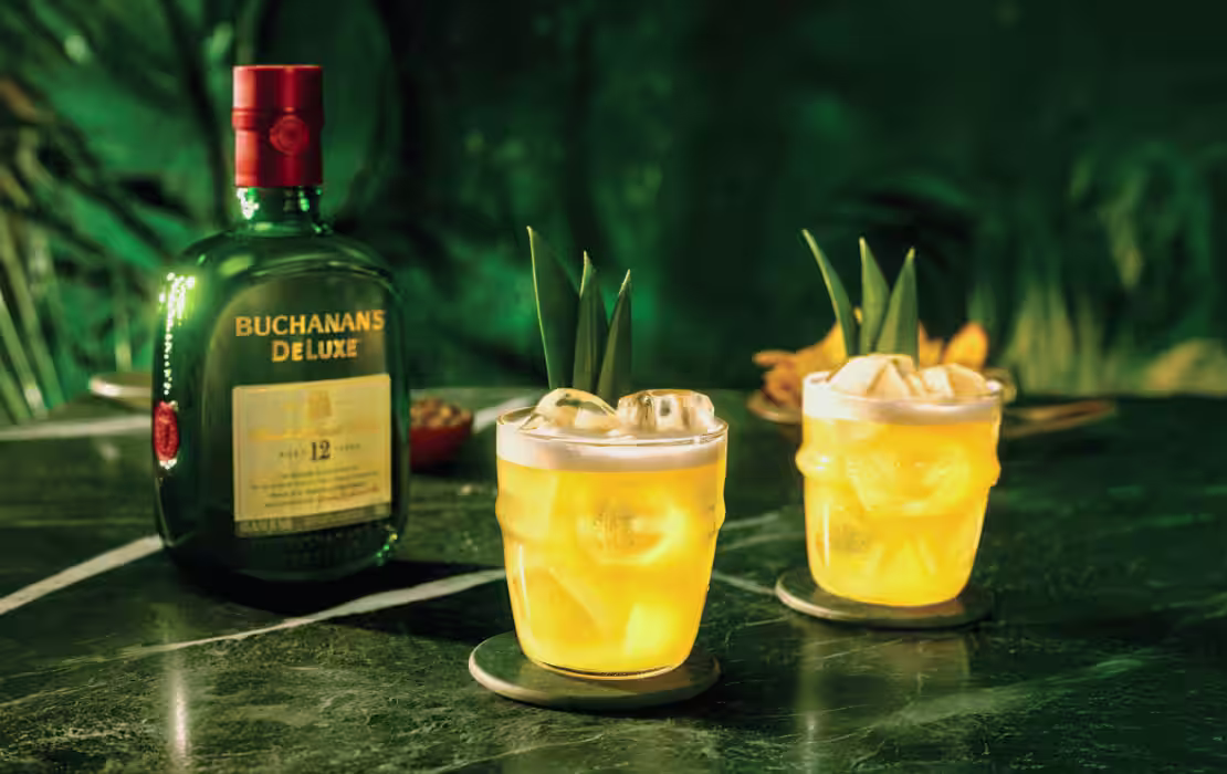 Two Buchanita cocktails on the rocks with pineapple garnish and a bottle of Buchanan's Deluxe Whiskey on a green marble counter