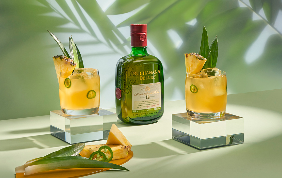 Two spicy piña margarita cocktails with a bottle of Buchanan's Deluxe in between the cocktails